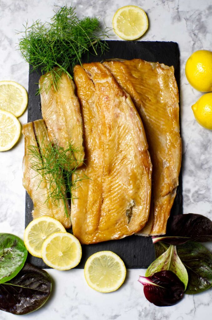 Black platter containing Smoked Trout garnished with lemon slices and fresh dill.