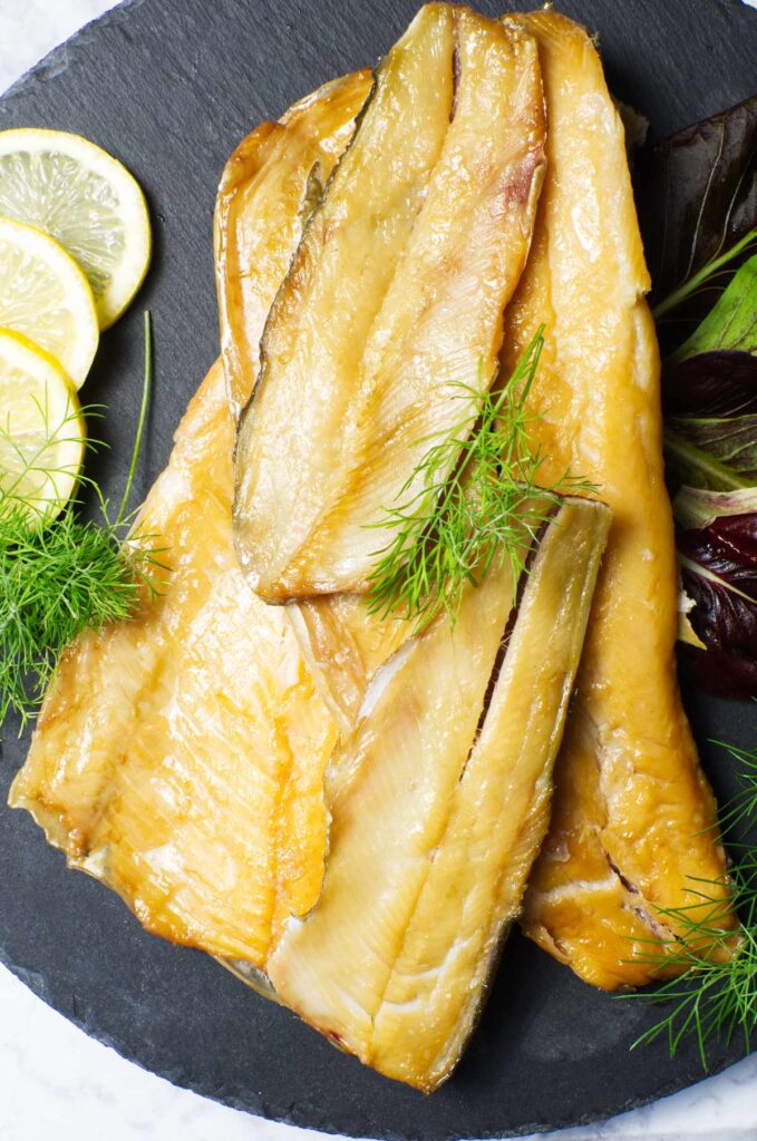 Black platter containing Smoked Trout garnished with lemon slices and fresh dill.