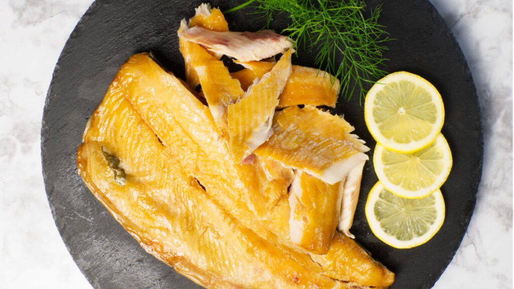 Black platter containing Smoked Trout garnished with lemon slices and fresh dill.