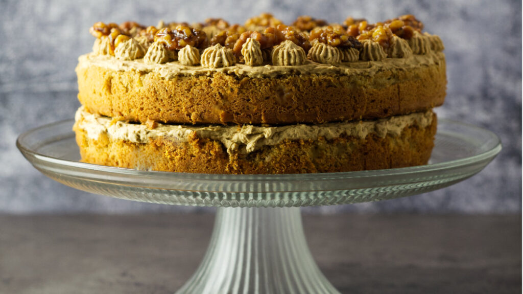 Coffee Walnut Sandwich showing the layers of sponge, buttercream and walnuts on top. The cake is on a glass cake stand.
