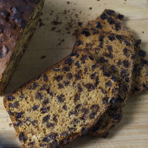 Wooden board with an Irish Tea Loaf in the background. In the foreground is an up close look at a slice of the bread.