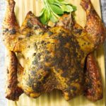 Wooden board with a whole Smoked Spatchcock Turkey on it, garnished with fresh sage.