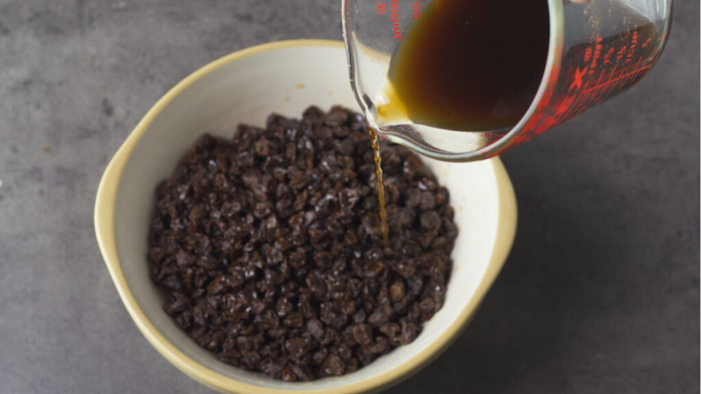 Bowl containing raisins and spices. Warm tea is being poured into the bowl.
