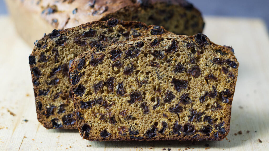Wooden board with an Irish Tea Loaf in the background. In the foreground  is an up close look at a slice of the bread.