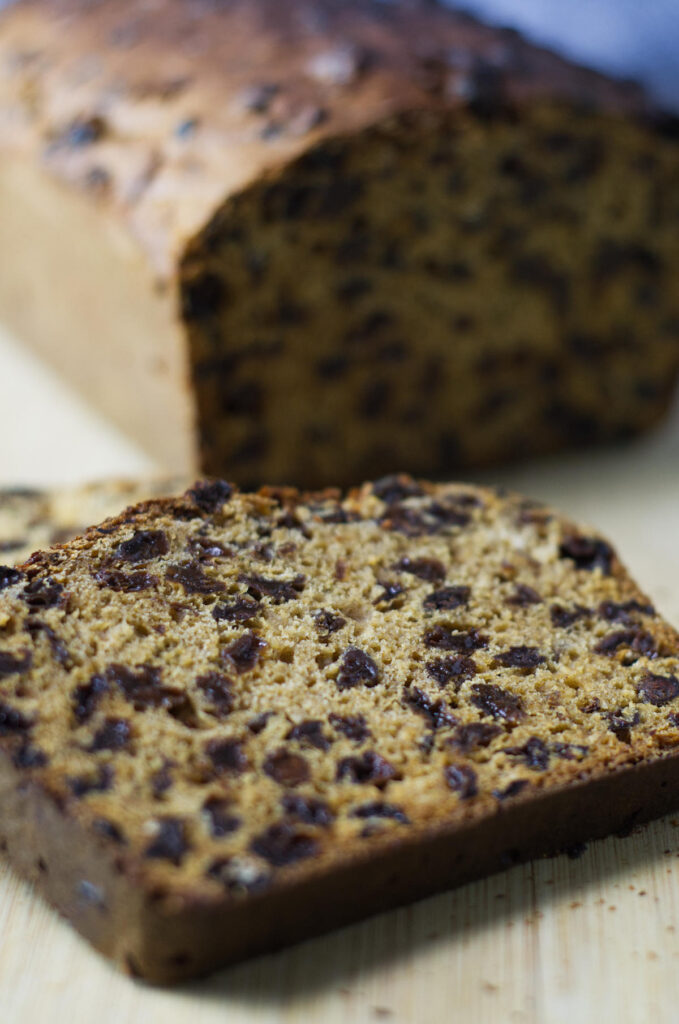 Wooden board with an Irish Tea Loaf in the background. In the foreground  is an up close look at a slice of the bread.
