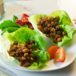 White plate with chorizo chickpeas lettuce cups on the plate with a tomato and parsley garnish.