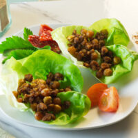 White plate with chorizo chickpeas lettuce cups on the plate with a tomato and parsley garnish.