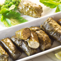 A long white plate containing stuffed grape leaves garnished with lemon wedges and parsley.