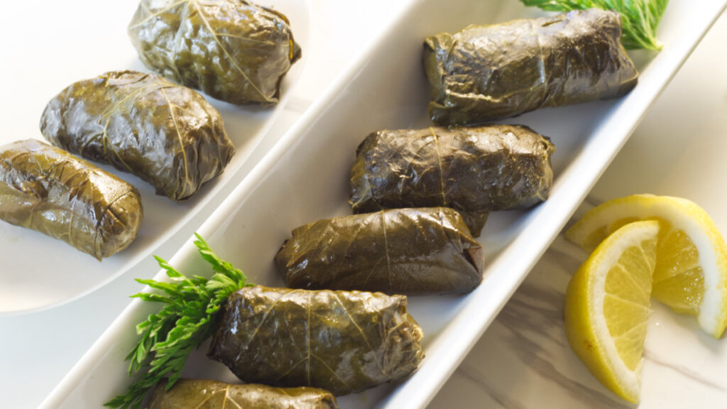 Two long white plates containing stuffed grape leaves garnished with lemon wedges and parsley. 