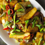 White oval dish containing the finished recipe of salt and chilli chips garnished with snipped spring onions.