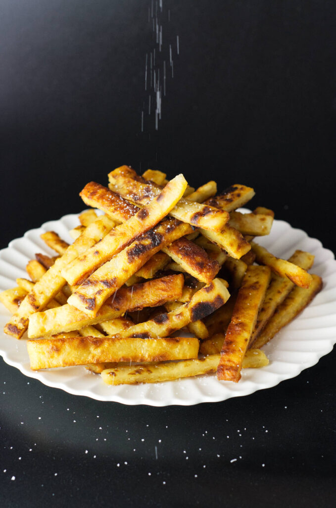 While plate containing a stacked portion of potato farl fries. Salt can be seen falling on the fries.
