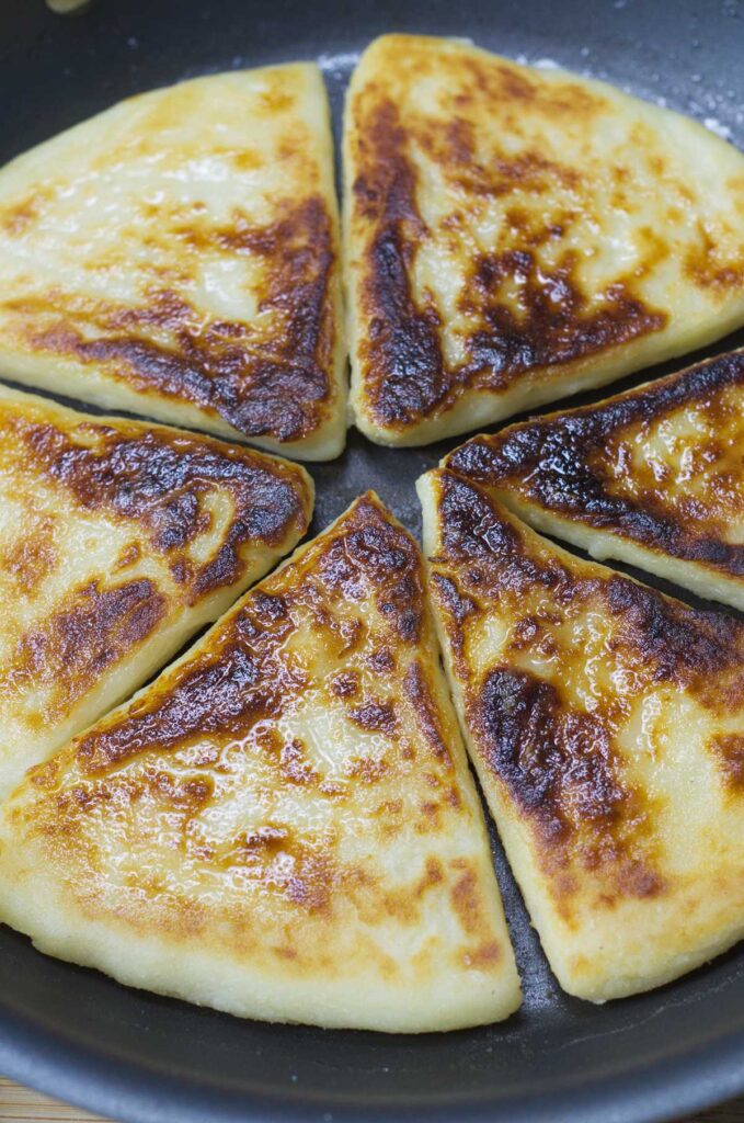 Griddle containing fried Potato Farls glistening with oil.