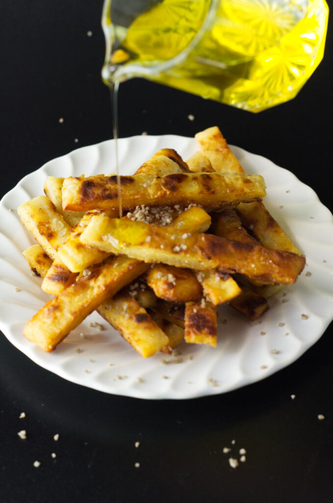 White plate with a heaped portion of potato farl fries. On them is smoked salt with truffle oil being poured over them.