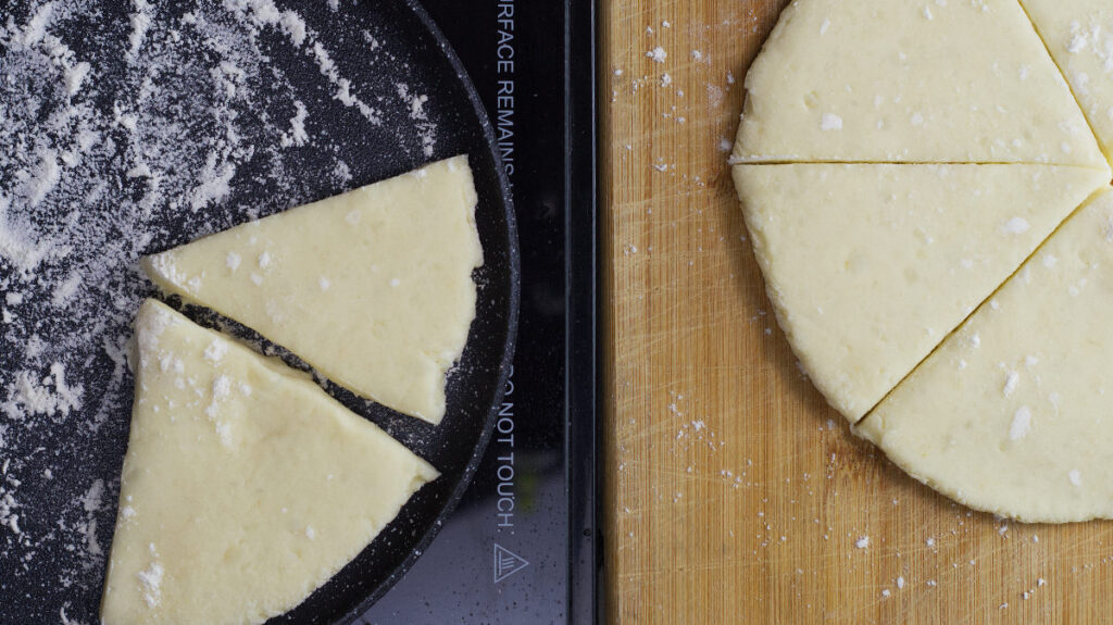 On the left is a griddle containing a couple of potato Farls that have been placed there. On the right is the wooden  board containing the rest of the farls.