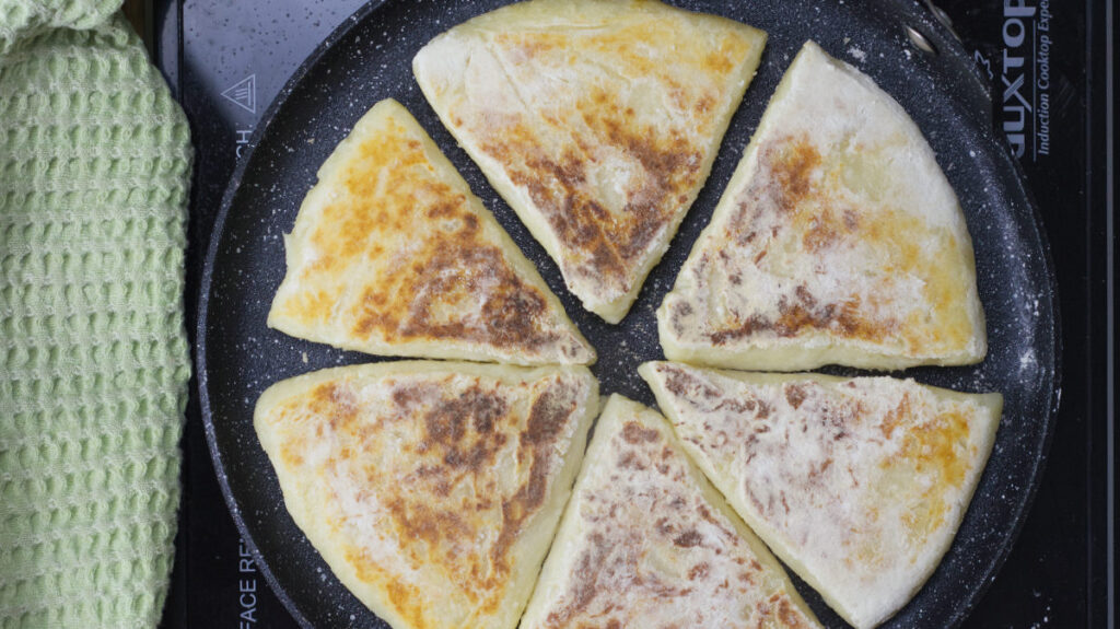 Griddle showing one side of the farls cooked. Resting at the side of the griddle is a green drying cloth.