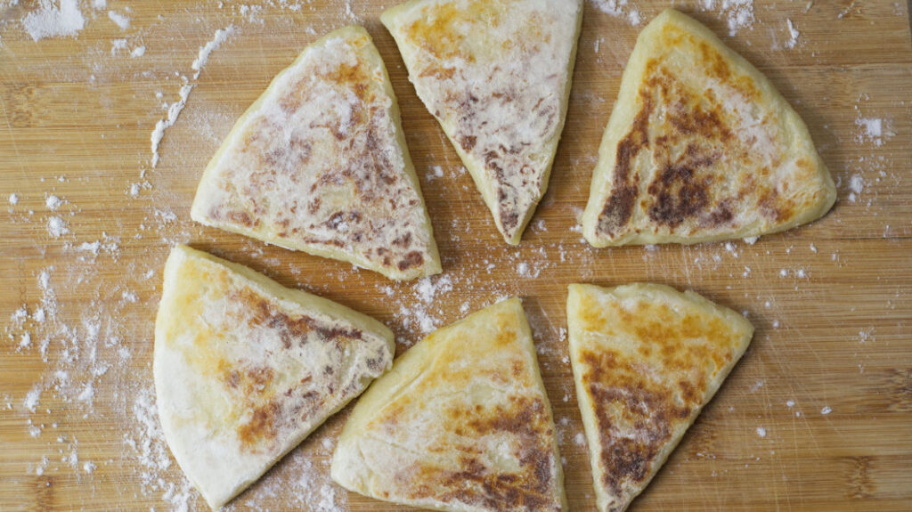 Wooden board with cooked potato farls on it with a dusting of flour on the board.
