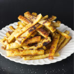 While plate containing a stacked portion of potato farl fries. Salt can be seen falling on the fries.