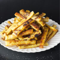 While plate containing a stacked portion of potato farl fries. Salt can be seen falling on the fries.